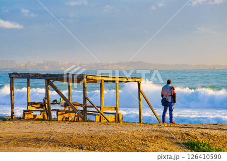 Male person relaxing on seashore, looking at waves Male person relaxing on seashore, looking at waves 126410590