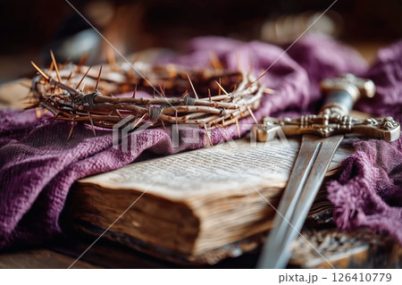 Religious Symbols Including a Thorn Crown and Sword on an Ancient Book With a Purple Cloth Background 126410779