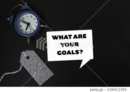Clock is on a table with a tag that says What are your goals Clock is on a table with a tag that says What are your goals 126411395