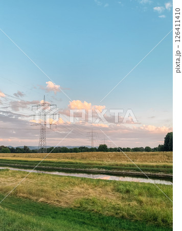 Field with a river running through it and a few power lines in the background 126411410