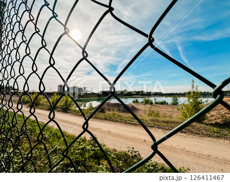A chain link fence with a view of a lake and a building in the background A chain link fence with a view of a lake and a building in the background 126411467