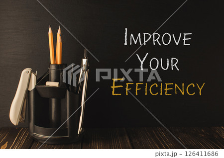 Pencil holder with a pair of pencils and a pen sits on a wooden table 126411686