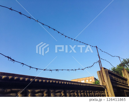 A wire fence with barbed wire is hanging over a wall 126411865