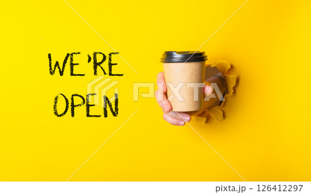 A person holding a coffee cup with the words We're open 126412297