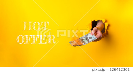 Person is holding a bill in a hole in a yellow background 126412301