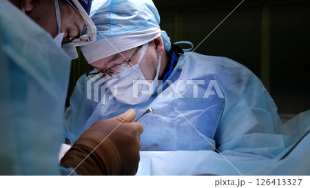 Surgical team performing intricate medical procedure, wearing protective gear, working collaboratively with focused precision inside sterile operating theater 126413327