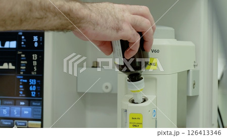 Surgical professional carefully filling anesthetic vaporizer, preparing patient for critical medical intervention in pristine operating theater environment 126413346