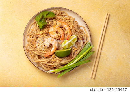 Bowl of pad thai noodles garnished with shrimps and lime on yellow background, traditional dish of Thailand 126413457