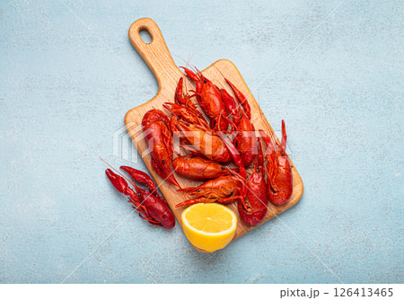 Cooked crayfish lying on wooden cutting board with lemon top view on blue background 126413465