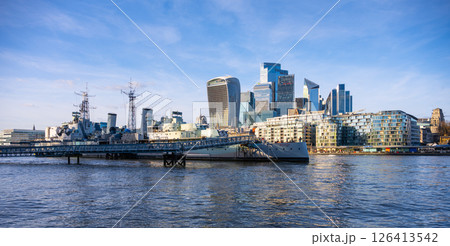 HMS Belfast is moored along the River Thames as modern buildings rise in the background. It showcases a blend of historic naval heritage and contemporary architecture in London. 126413542