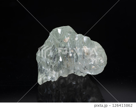 A transparent, light green beryl crystal sits prominently on a dark, rocky base with internal inclusions visible, displaying angular facets and a somewhat uneven, natural shape A transparent, light green beryl crystal sits prominently on a dark, rocky base with internal inclusions visible, displaying angular facets and a somewhat uneven, natural shape 126413862