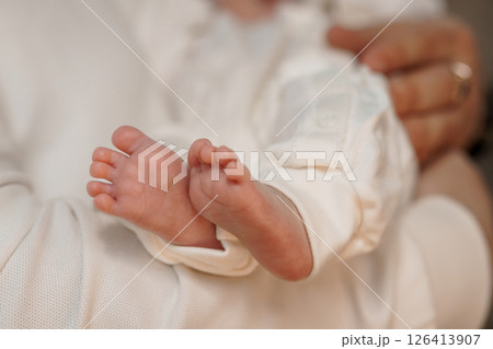Close-up of tiny newborn baby feet held gently in loving hands, wrapped in soft white fabric, representing tenderness, new life, and parental care in a peaceful setting Close-up of tiny newborn baby feet held gently in loving hands, wrapped in soft white fabric, representing tenderness, new life, and parental care in a peaceful setting 126413907