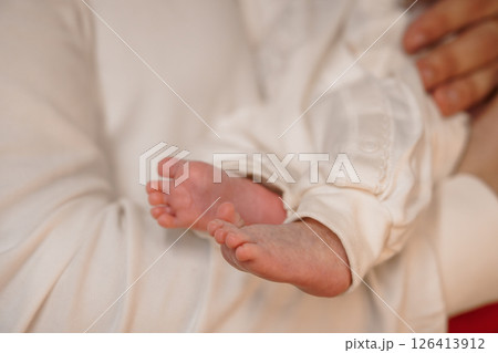 Tender moment of a newborn baby's tiny feet held gently in a parent's hands, showcasing a soft white garment and intimate connection infant, parenthood, love 126413912