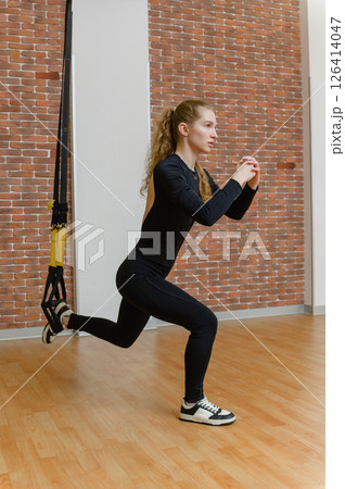 Fit woman doing suspension lunge exercise in gym. 126414047