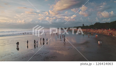 Tourists walking along the sandy shore at Dreamland Beach in Bali, Indonesia, are captured in an aerial drone view during a stunning sunset, surrounded by a dramatic, cloud-filled sky Tourists walking along the sandy shore at Dreamland Beach in Bali, Indonesia, are captured in an aerial drone view during a stunning sunset, surrounded by a dramatic, cloud-filled sky 126414063
