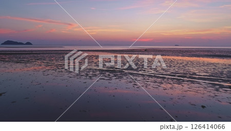 Aerial view of beautiful sunset reflecting on the wet sand of a tropical beach at low tide, creating a colorful and serene atmosphere with islands visible on the horizon Aerial view of beautiful sunset reflecting on the wet sand of a tropical beach at low tide, creating a colorful and serene atmosphere with islands visible on the horizon 126414066