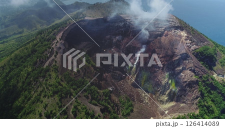 White smoke is rising from the crater of Mount Iya volcano, located near Ende on Flores island, Indonesia, surrounded by lush green vegetation and overlooking the ocean 126414089