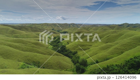 Rolling green hills extend as far as the eye can see across the landscape of Sumba island, Indonesia, with a line of trees growing along a valley and a partly cloudy sky overhead Rolling green hills extend as far as the eye can see across the landscape of Sumba island, Indonesia, with a line of trees growing along a valley and a partly cloudy sky overhead 126414096