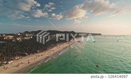 Aerial view of Cagban Beach in Boracay, Philippines during a vibrant sunset, showing tourists swimming, sunbathing, and enjoying watersports activities along the picturesque coastline 126414097