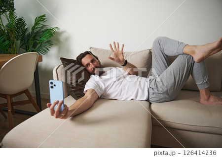 Casual Man Relaxing at Home While Interacting Through Video Call on Sofa 126414236