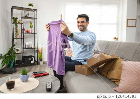 Man opens the cardboard package and looks at the new T-shirt Man opens the cardboard package and looks at the new T-shirt 126414393
