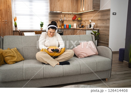 Competitive woman with wireless headphones playing video game at home 126414408