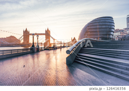 Morning sunlight bathes Tower Bridge in golden hues, viewed from The Queen's Walk in London. The tranquil atmosphere is enhanced by the calm river and modern architecture nearby. Morning sunlight bathes Tower Bridge in golden hues, viewed from The Queen's Walk in London. The tranquil atmosphere is enhanced by the calm river and modern architecture nearby. 126416356