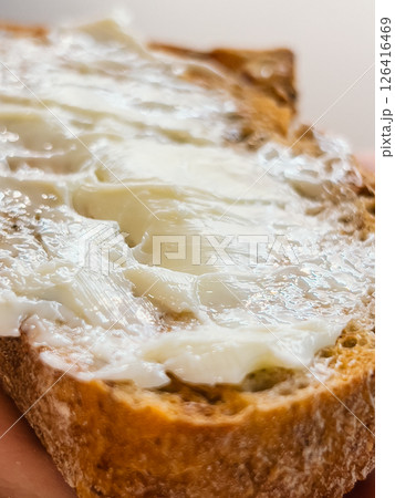 Butter melts on rustic slice, butter adds richness to natural texture, butter spread closeup shows warm homemade feel, bread captures cozy breakfast essence. Spread of creamy butter on crusty slice  126416469