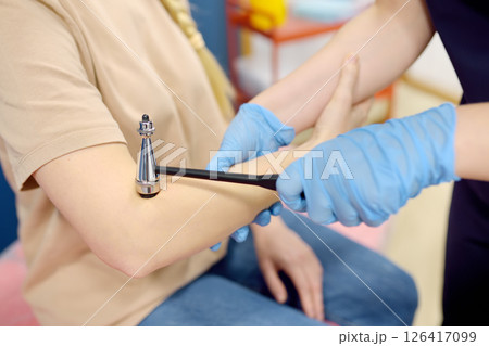 A neurologist doctor examining elbow reflex of young female patient. 126417099