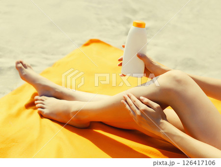 Summer vacation, close up of woman sunbathing and applying suntan cream on her legs lying on beach Summer vacation, close up of woman sunbathing and applying suntan cream on her legs lying on beach 126417106