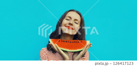 Summer portrait of happy young woman eating fresh slice of watermelon fruit on blue background 126417123