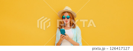 Summer portrait of happy young woman with mobile phone looking at device on yellow background Summer portrait of happy young woman with mobile phone looking at device on yellow background 126417127