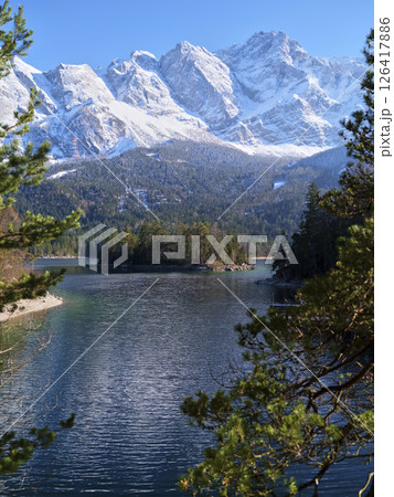 Majestic snow-capped mountains overlook a serene lake surrounded by lush greenery in a peaceful setting Majestic snow-capped mountains overlook a serene lake surrounded by lush greenery in a peaceful setting 126417886