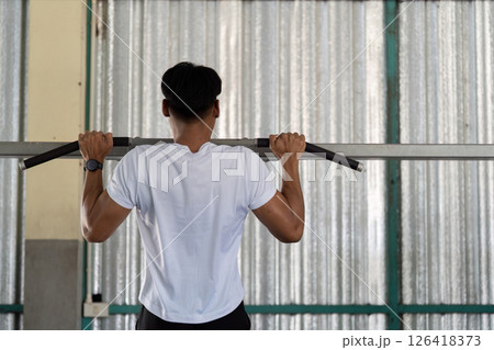 Wellness and Fitness. Young man doing pull-ups in gym for strength training. Wellness and Fitness. Young man doing pull-ups in gym for strength training. 126418373