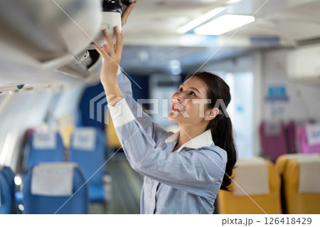 Business travel: Asian woman happily organizing luggage in plane 126418429