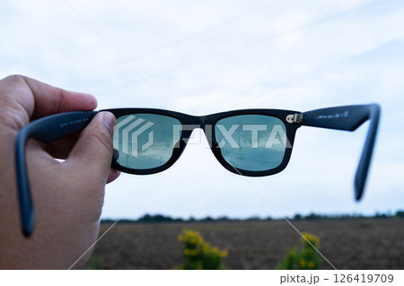 Hand holding stylish sunglasses outdoor field product bright day close-up view 126419709