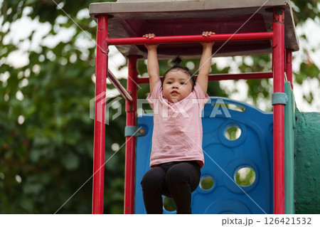 happy toddler girl hanging the red bar by her hand at outdoor playground in park happy toddler girl hanging the red bar by her hand at outdoor playground in park 126421532