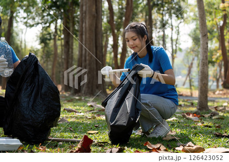 Sustainable Practices and Volunteering. A young woman actively participates in a community cleanup, collecting waste for a greener future. 126423052