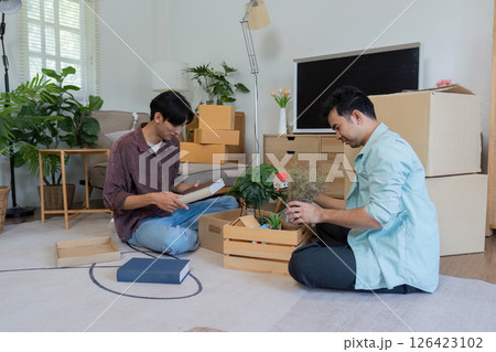 Gay couple unpacking boxes and arranging plants in their new home. Gay couple unpacking boxes and arranging plants in their new home. 126423102