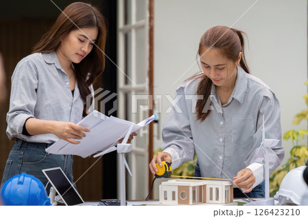 Sustainability and Architectural Design. Two women collaborating on a sustainable building model, discussing eco-friendly solutions. 126423210