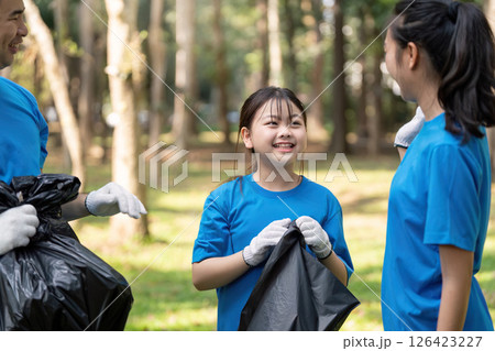 Engaged family volunteers discussing their garbage collection efforts in a park, promoting teamwork and environmental care. Engaged family volunteers discussing their garbage collection efforts in a park, promoting teamwork and environmental care. 126423227