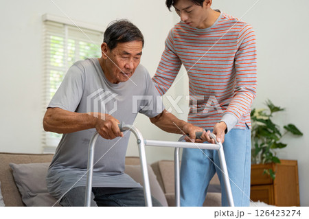 Young man assisting his elderly father with a walker for mobility support. Young man assisting his elderly father with a walker for mobility support. 126423274