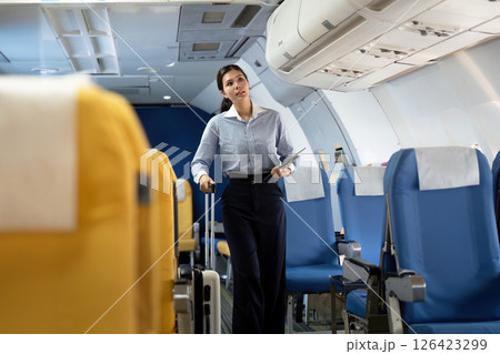 Business travel: Flight attendant assisting a young woman with luggage in airplane 126423299
