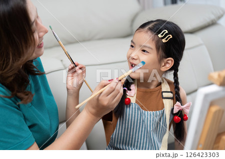 Mother applying paint on daughter face while painting together Mother applying paint on daughter face while painting together 126423303