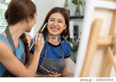 Lesbian couple sharing laughter while painting at home 126423304