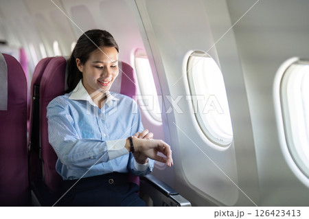 Business travel: Smiling woman checking her watch on airplane 126423413