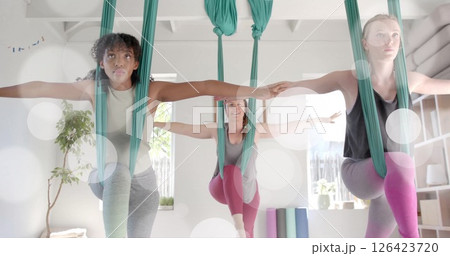 Image of light spots over diverse female instructor and teenage girls practicing aerial yoga 126423720