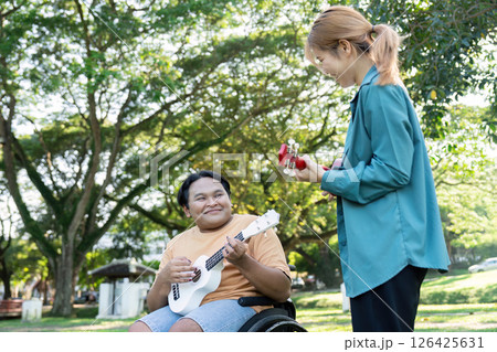 Young man in a wheelchair smiling while playing ukulele with a friend. Young man in a wheelchair smiling while playing ukulele with a friend. 126425631