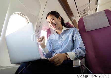 Business travel: Young woman celebrating success on laptop in flight 126425640
