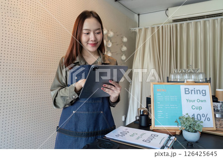 Technology and Cafe Management. A barista manages orders using a tablet in a cozy cafe ambiance. 126425645